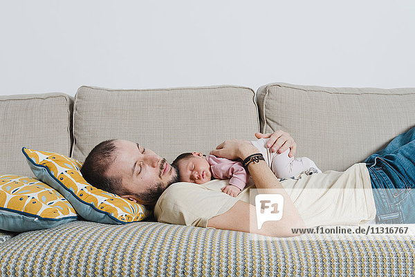 Vater und seine neugeborene Tochter schlafen auf der Couch.
