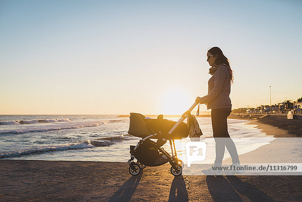 Woman walking with a stroller on the seashore at sunset