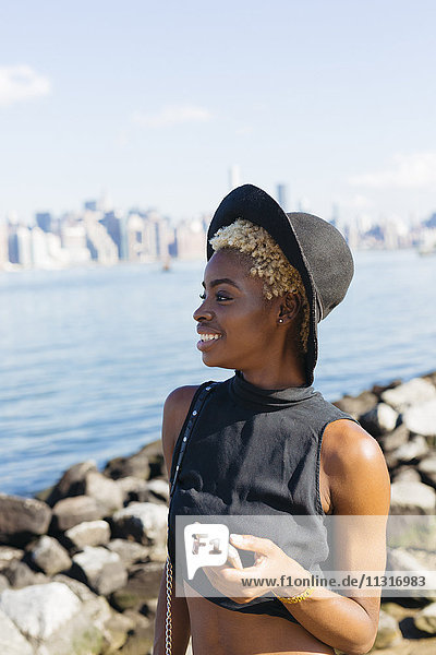 USA  New York City  Brooklyn  smiling young woman at East River with cell phone