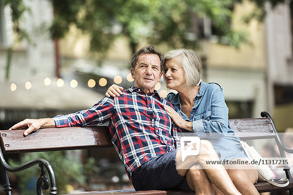 Seniorenpaar sitzt auf der Bank und schaut sich etwas an.