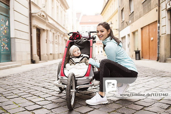 Mother in sportswear with child in stroller in the city