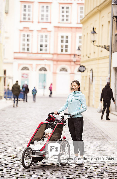 Mutter in Sportbekleidung mit Kind im Kinderwagen in der Stadt