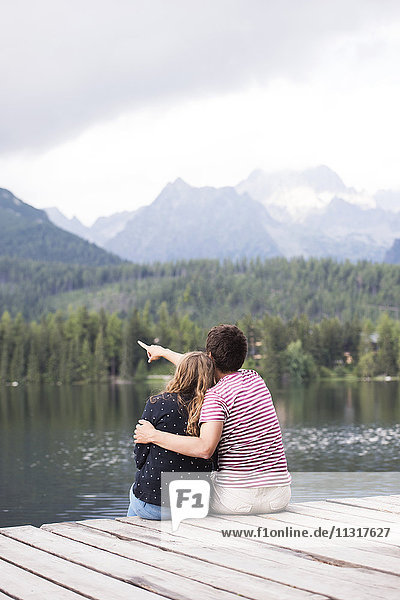 Rückansicht eines jungen Paares auf einem Steg am See