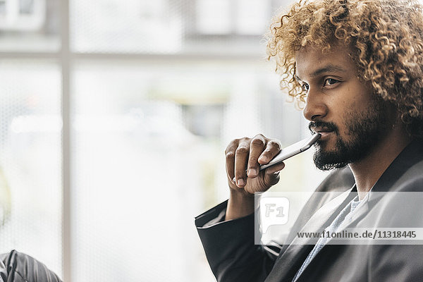 Young businessman holding smart phone  looking thoughtful