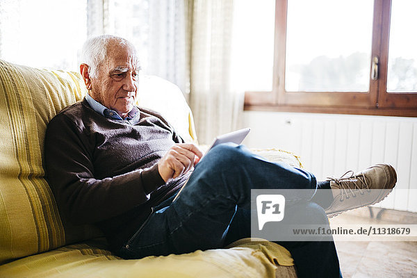 Älterer Mann auf der Couch sitzend mit Tablette