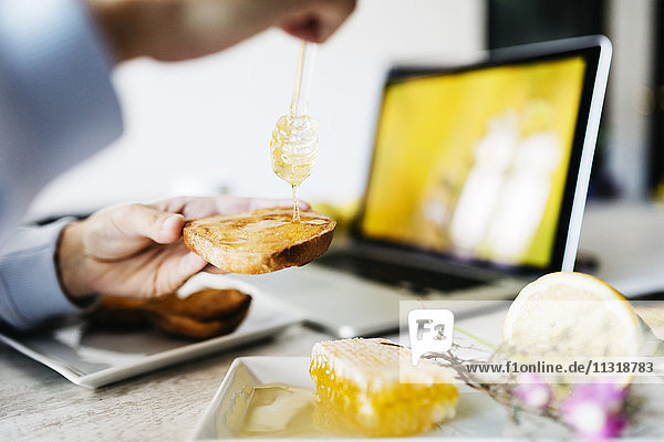 Frau tropft Honig auf Toast an seinem Arbeitsplatz  Nahaufnahme