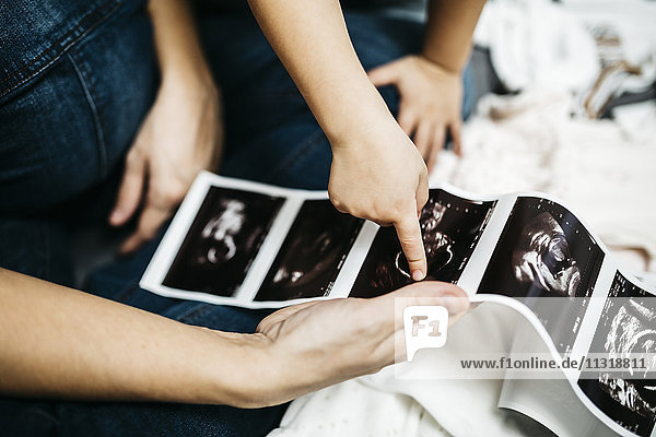Kleiner Junge beim Betrachten der Ultraschallaufnahmen seiner schwangeren Mutter  Teilansicht