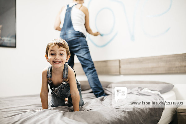 Porträt eines kleinen Jungen  der auf dem Bett spielt  während seine Mutter die Wand malt.
