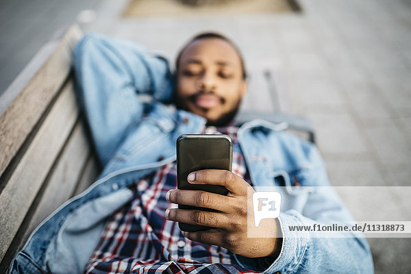 Young man lying on bench looking at cell phone  close-up