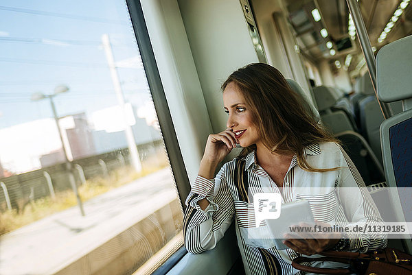 Lächelnde Frau im Zug mit Tablette