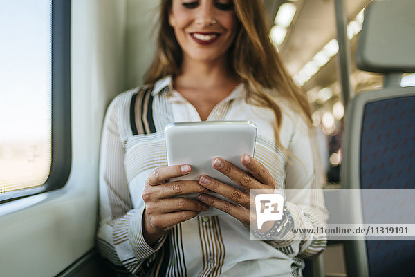 Lächelnde Frau im Zug mit Tablette