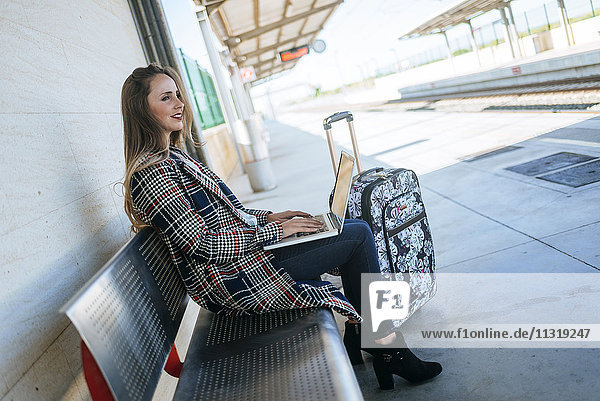 Geschäftsfrau sitzt auf einer Bank am Bahnhof mit einem Laptop