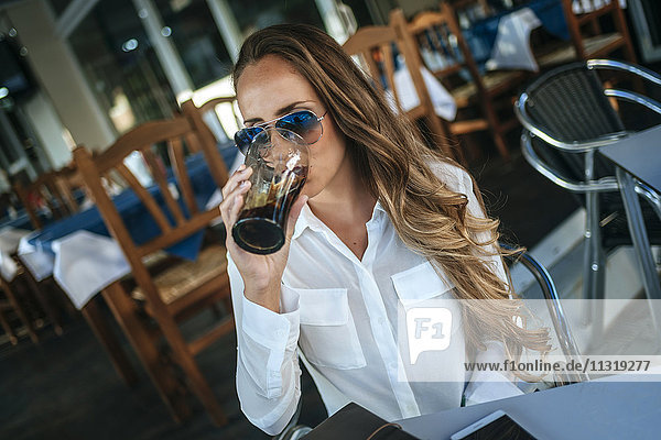 Eine Frau trinkt eine Cola in einem Straßencafé.