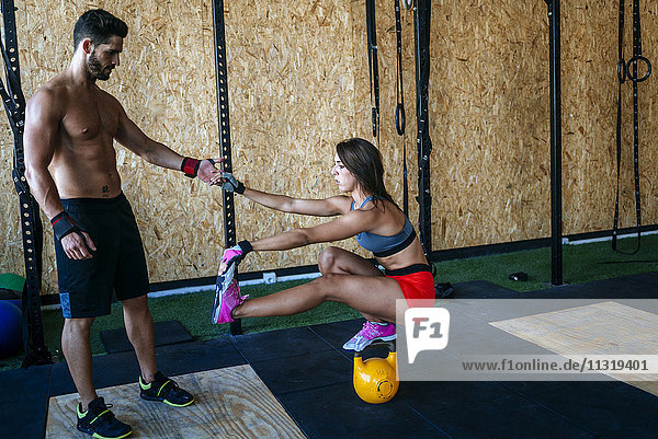 Man helping woman keeping balance on a kettlebell in gym