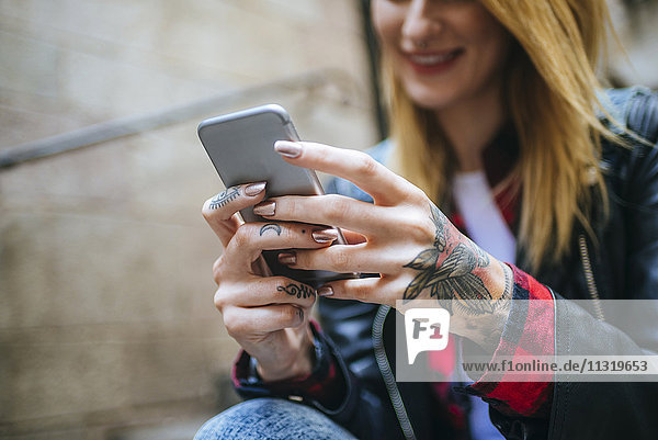 Tattooed woman's hands holding cell phone  close-up
