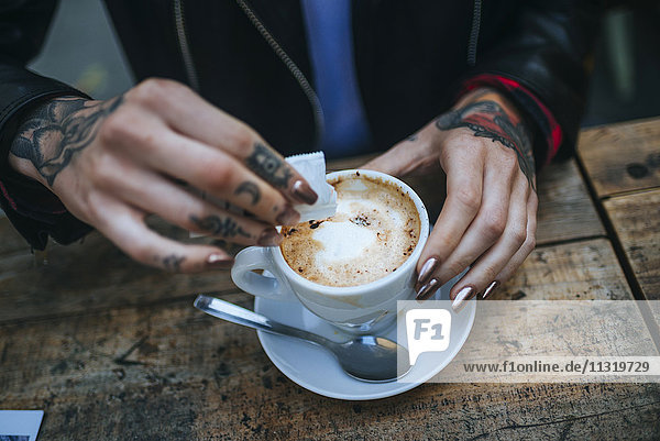 Woman's tattooed hands pouring sugar into cup of coffee  close-up