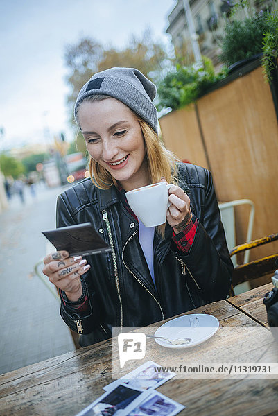 Young tattooed woman sitting in a pavement cafe looking at photos