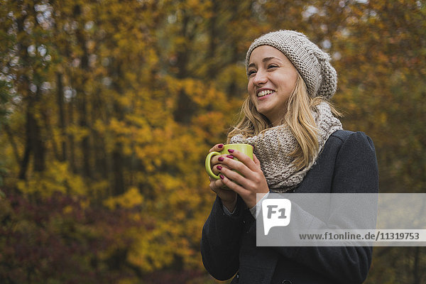 Lächelnde junge Frau mit Heißgetränk im Herbstwald