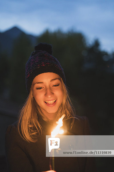 Lächelnde junge Frau  die in der Abenddämmerung ein Licht leuchtet.