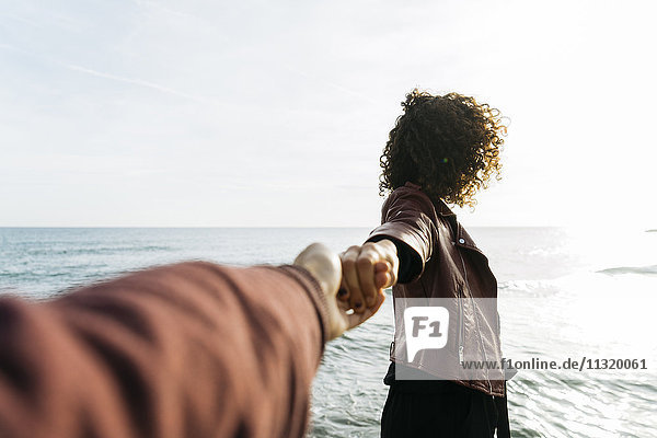 Frau vor dem Meer hält Hand mit ihrer Freundin
