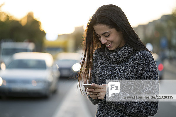 Lächelnde junge Frau mit Handy auf der Straße