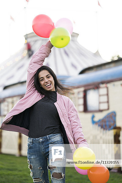 Glückliche junge Frau hält Luftballons im Freien.