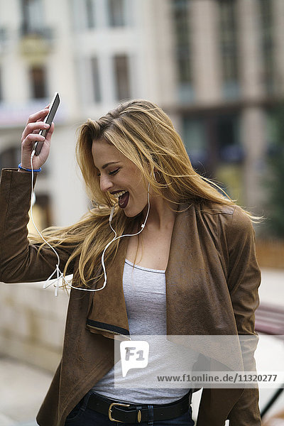 Glückliche junge Frau beim Musikhören mit Kopfhörer und Smartphone
