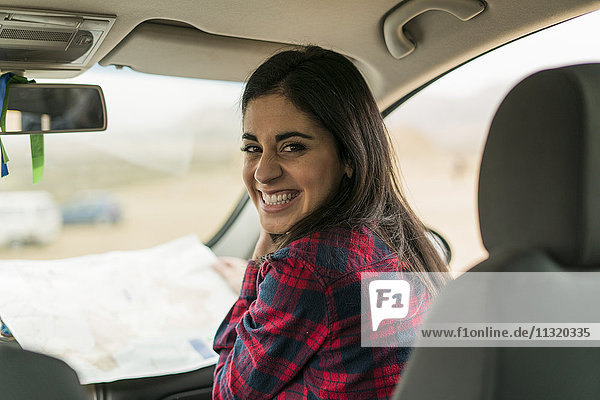 Porträt der lachenden jungen Frau mit Karte im Auto