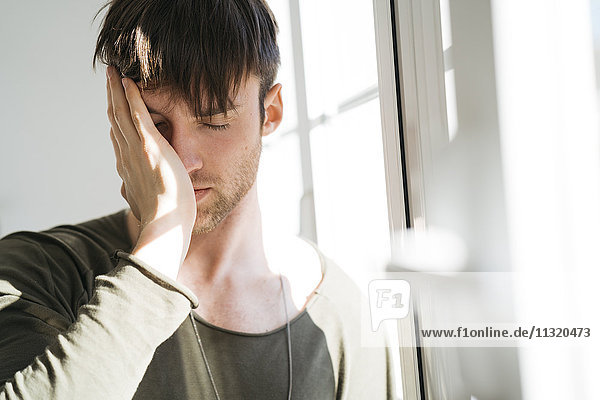 Young man with eyes closed and hand on his face