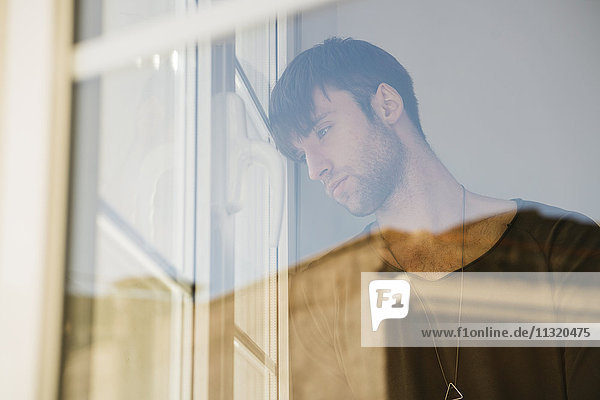Sad young man looking through window
