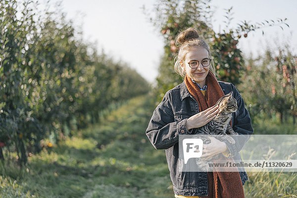 Young woman holding a cat in apple orchard