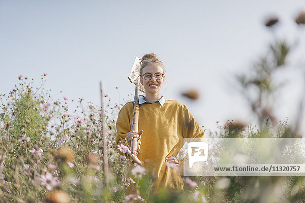 Lächelnde junge Frau mit Spaten im Bauerngarten
