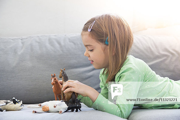 Little girl lying on couch playing with animal figurines