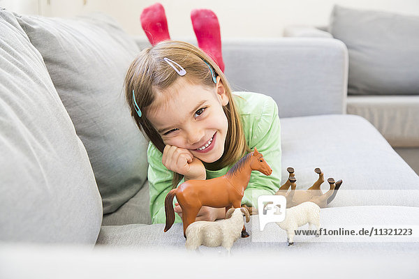 Portrait of smiling little girl lying on couch with her animal figurines