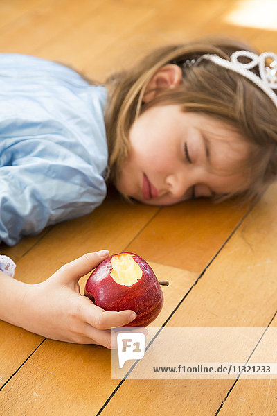 Kleines Mädchen auf Holzboden liegend mit gebissenem roten Apfel