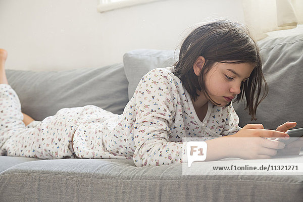Girl lying on the couch using mini tablet