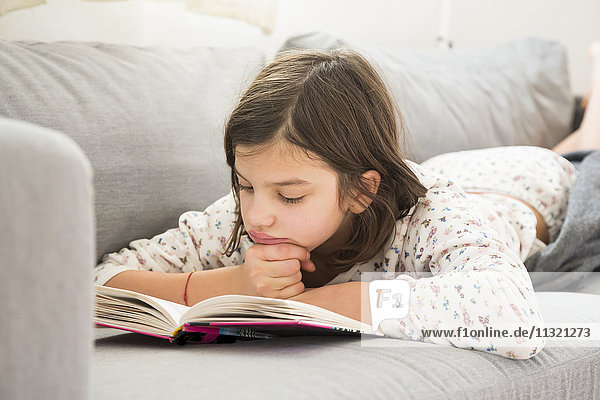Girl lying on the couch reading a book
