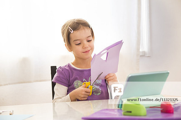 Kleines Mädchen,  das zu Hause klimpert,  schneidet Papier mit Online-Hinweisen.