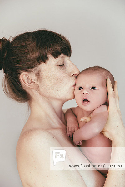 Nude mother kissing her newborn baby
