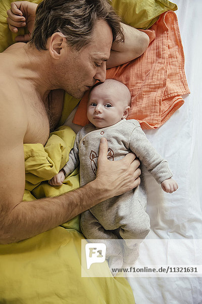 Vater kuschelt im Bett mit seinem neugeborenen Baby