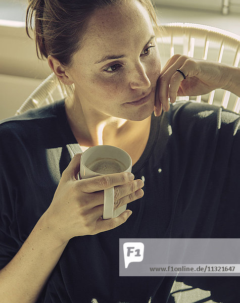 Pensive young woman sitting in a chair with coffee mug