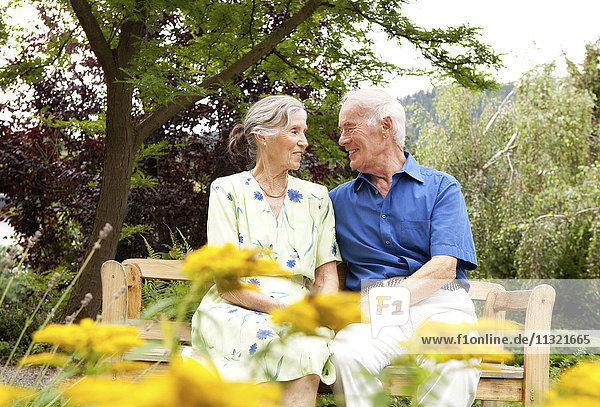 Zuversichtliches Seniorenpaar sitzt auf der Bank im Garten