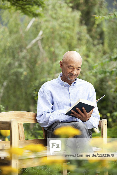 Senior man sitting on garden bench reading book