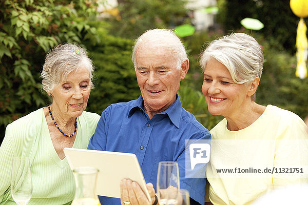 Älterer Mann beim Betrachten des digitalen Tabletts mit Gästen