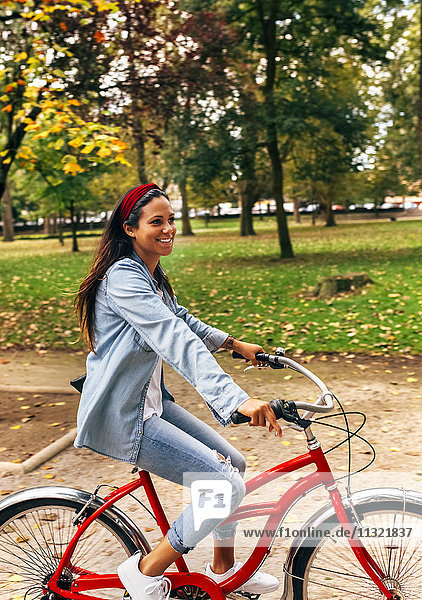 Smiling young woman riding a bike in a park