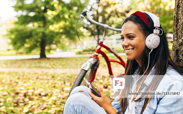 Junge Frau  die im Herbst mit ihrem Smartphone im Park Musik hört.