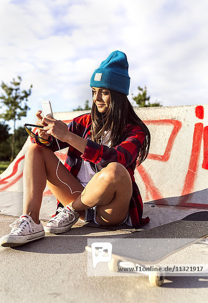 Young woman with skateboard and cell phone in a skatepark