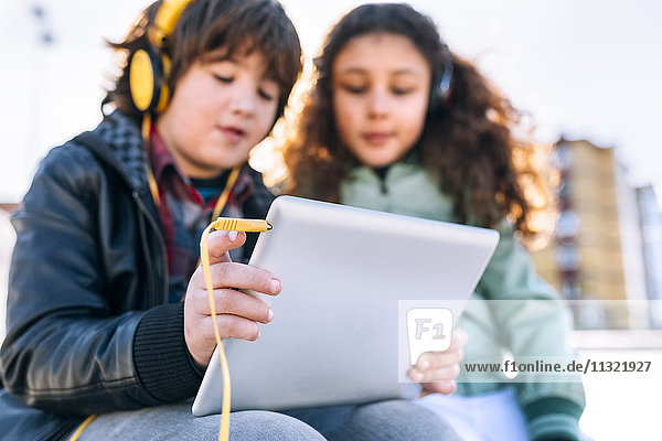 Zwei Kinder beim Musikhören mit Kopfhörer und Tablett