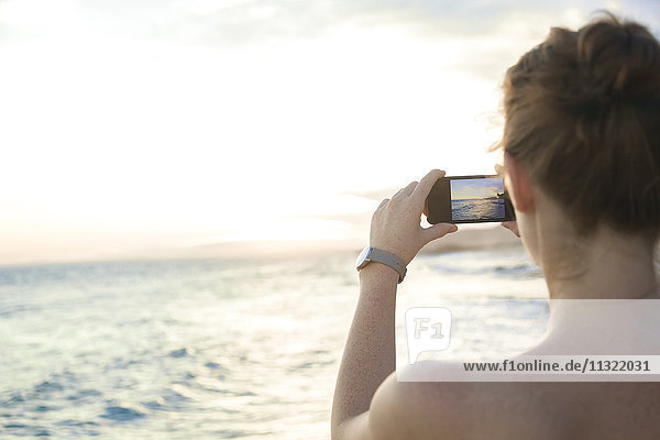 Frau am Strand fotografiert mit ihrem Smartphone
