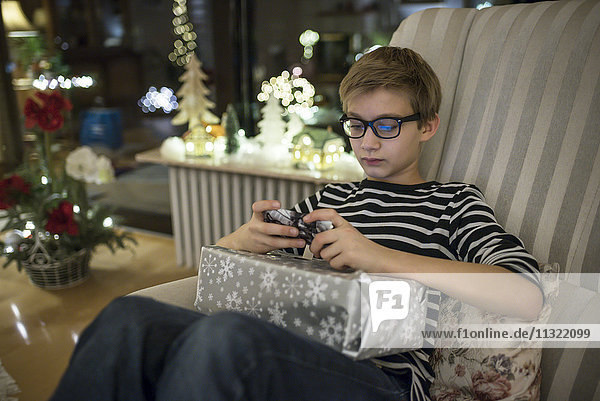 Schenken am Weihnachtsabend  Junge zahlt mit Smartphone mit Geschenk auf dem Schoß